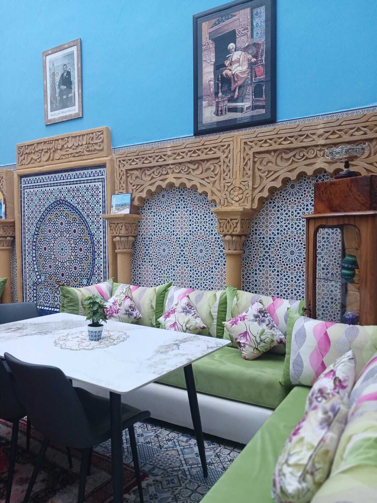 Ein Zimmer mit blauer Wand, einem gemusterten Sofa, einem Tisch mit Stühlen und dekorativen Wandpaneelen.