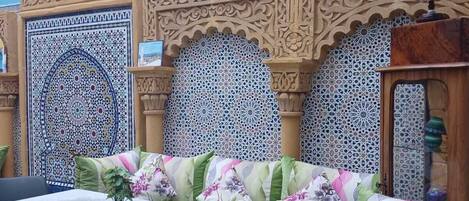 Una habitación con pared azul, un sofá estampado, una mesa con sillas y paneles decorativos.