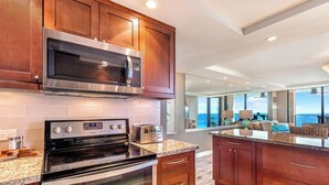 Una cocina moderna con microondas, estufa y tostadora, armarios de madera y un gran ventanal con vista al océano.