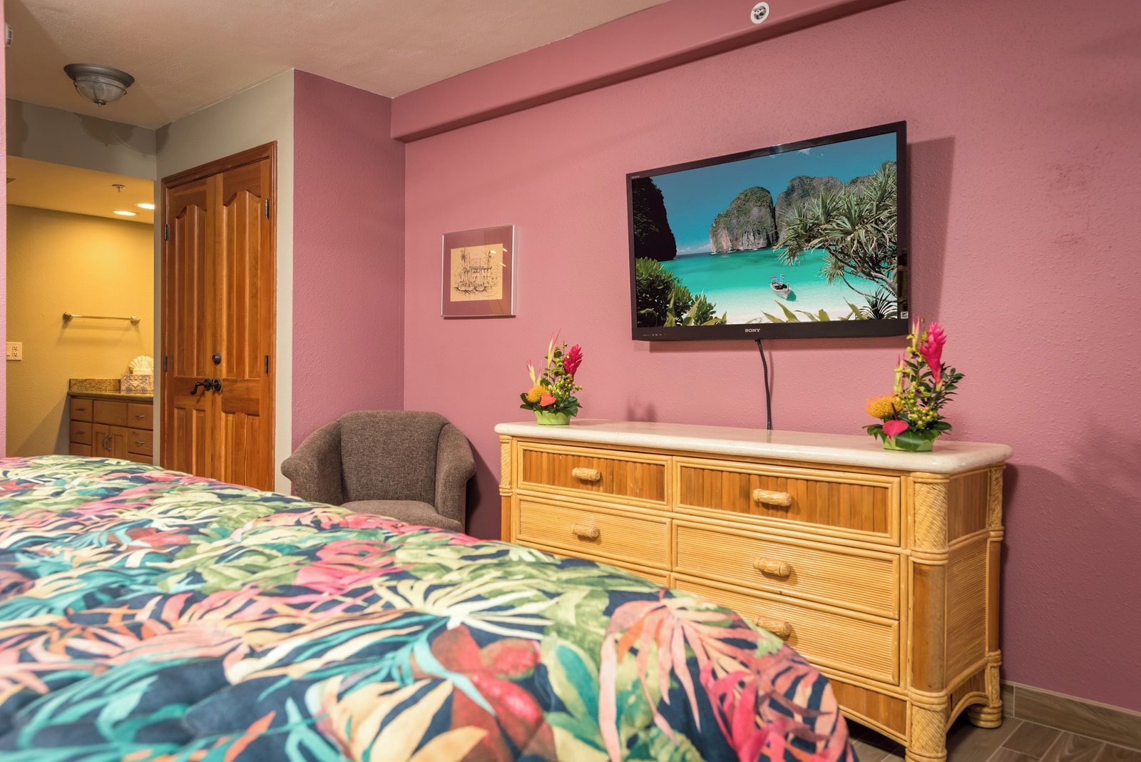 Een slaapkamer met een bed, een stoel, een dressoir, een televisie aan de muur en een schilderij.