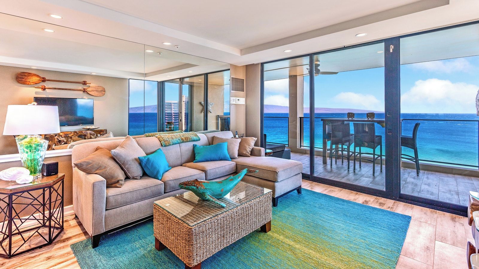 A modern living room with a large sofa, a coffee table, and a view of the ocean through large sliding doors.