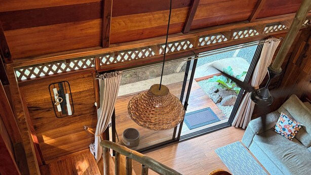 Un escalier en bois mène à une pièce où l’on trouve un luminaire suspendu, un canapé et une vue sur l’extérieur.