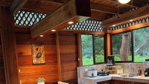 Un coin repas en bois avec une table dressée pour six personnes, une cuisine équipée d’une machine à café et une vue sur la verdure environnante.