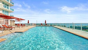 A swimming pool with lounge chairs and umbrellas, surrounded by a high-rise building with balconies. - Bay View 2BR at The Arya Coconut Grove (Miami)
