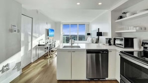 Una cocina moderna con armarios blancos, electrodomésticos de acero inoxidable y un amplio ventanal con vistas al cielo.