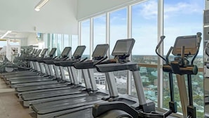 Una fila de cintas de correr en un gimnasio con amplios ventanales que dan a una vista de la ciudad.