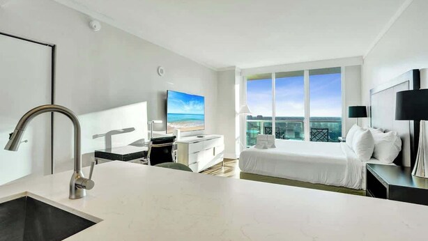 Habitación de hotel moderna con una cama grande, un escritorio, un lavamanos y un ventanal con vistas a la ciudad.