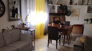 Un salon avec un canapé à rayures, une table à manger avec des chaises, une cheminée et un grand miroir au mur.