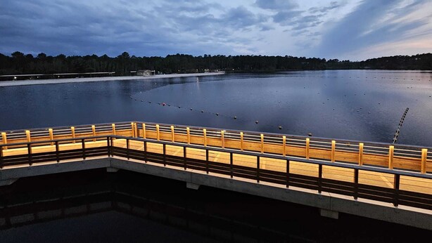 A calm lake with a wooden dock and a bridge.