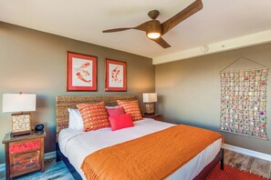 A bedroom with a bed, two wall-mounted lamps, a ceiling fan, framed artwork, and a wall decoration. - Mahana Villas | Oceanfront 6 BR Sleeps 17 | Car Incl. w/ 6+ Nights | MAH ML-3884 by KBM (Lahaina)