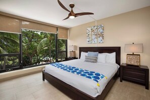 Quarto com uma cama grande, ventoinha no teto, janela com vista para árvores e obras de arte na parede.