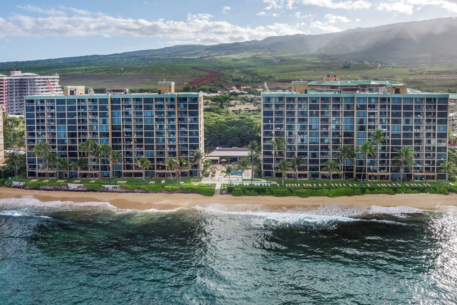 A beachfront hotel with multiple high-rise buildings, a beach, and a mountainous backdrop.