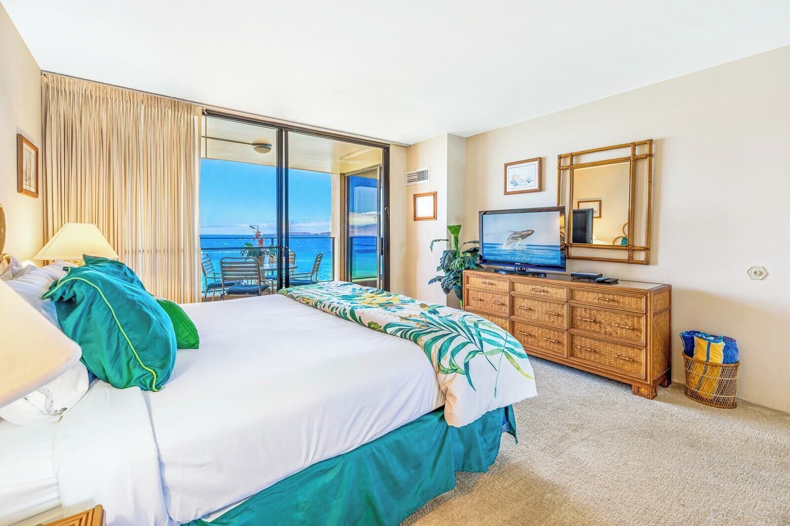 Ein Hotelzimmer mit Bett, Fernseher, Kommode und einem Balkon mit Meerblick.