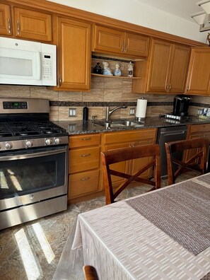 A kitchen with wooden cabinets, a microwave, stove, sink, and a dining area with a table and chairs. - Quiet cozy 2-bedroom apartment with AC in vibrant Skokie (Skokie)
