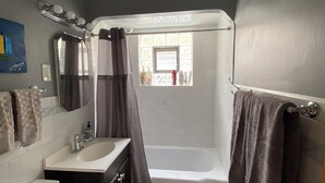 Een badkamer met toilet, wastafel, badkamermeubel, bad en douchegordijn.
