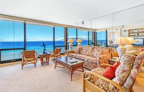 A spacious living room with large windows, a sofa, chairs, a coffee table, and a television. - Mahana Villas | Oceanfront 7 BR Sleeps 21 | Car Incl. w/ 6+ Nights | MAH ML-3890 by KBM (Lahaina)