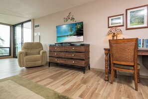 A living room with a sofa, a TV, a wicker side table, a chair, and a bookshelf. - Mahana Villas | Oceanfront 7 BR Sleeps 21 | Car Incl. w/ 6+ Nights | MAH ML-3890 by KBM (Lahaina)