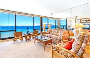 A spacious living room with a large view of the ocean, furnished with wicker chairs, a sofa, and a coffee table. - Mahana Villas | Oceanfront 7 BR Sleeps 23 | Car Incl. w/ 6+ Nights | MAH ML-3893 by KBM (Lahaina)
