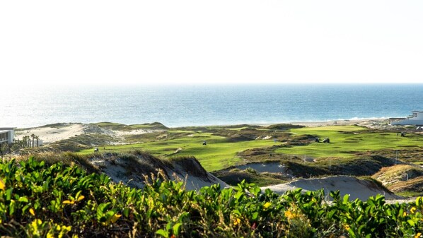 Un campo de golf costero con dunas de arena, un edificio y vista al océano.