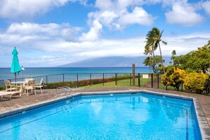 A swimming pool with a view of the ocean and mountains, surrounded by a fence and outdoor seating. - Napili Point | Oceanfront 3 BR, Sleeps 12 | Car Incl. w/ 6+ Nights | NAP ML-3924 by KBM (Lahaina)