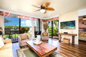 A spacious living room with a wooden coffee table, comfortable seating, a ceiling fan, and large windows offering a view of the outdoors. - Napili Point | Oceanfront 3 BR, Sleeps 12 | Car Incl. w/ 6+ Nights | NAP ML-3924 by KBM (Lahaina)