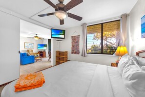 A hotel room with a bed, a television, a ceiling fan, a window with curtains, and a view of the outdoors. - Napili Point | Oceanfront 3 BR, Sleeps 12 | Car Incl. w/ 6+ Nights | NAP ML-3924 by KBM (Lahaina)