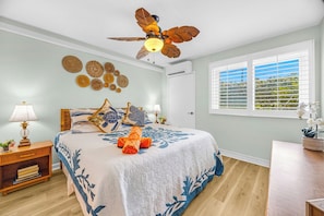 Ein Schlafzimmer mit Bett, Deckenventilator, Fenster mit Jalousien und Wanddekoration.
