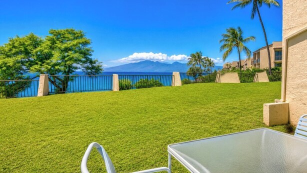 Eine grüne Außenausstattung mit Blick auf das Meer und die Berge, ein Metalltisch und Stühle.