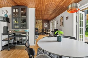 A modern kitchen with a dining area, wooden ceiling, and a view of the outdoors.
