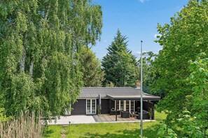 A modern building with a metal roof, large windows, and a patio area with outdoor seating. - Cozy holiday home in peaceful Bredfjed (Rødby)