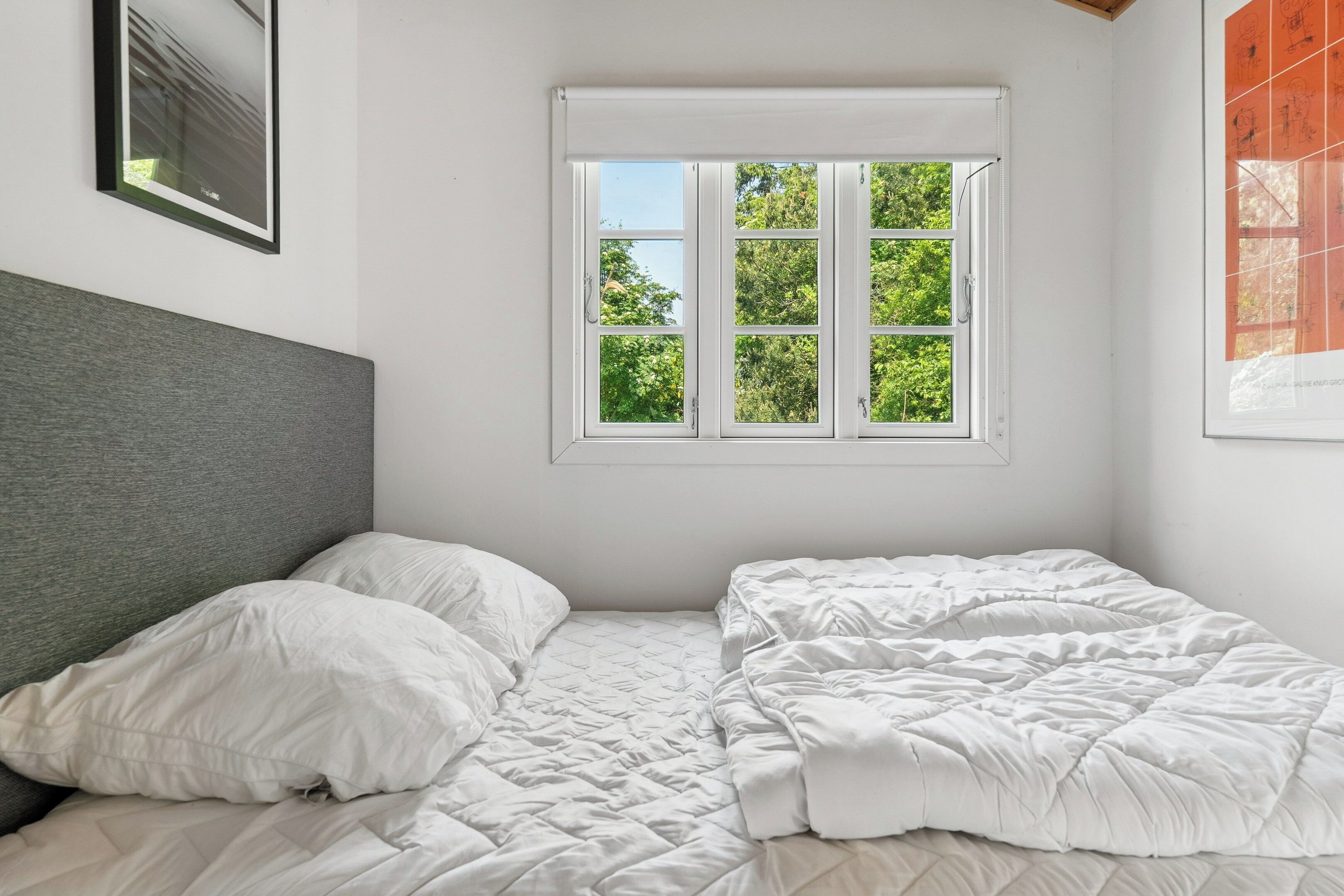 A bedroom with a bed, a window with a view of trees, and a framed picture on the wall.