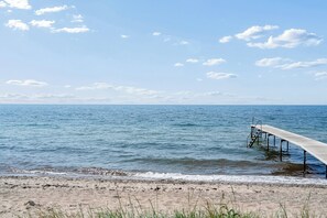 A beach with a wooden pier extending into calm waters, a sandy shore, and a clear sky.