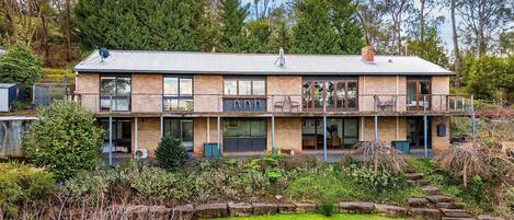 Une maison à deux étages avec un balcon, de grandes fenêtres et un jardin.