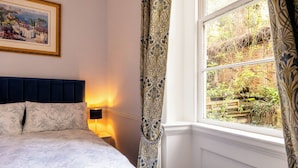 Una camera da letto con un letto, un comodino, una lampada, una finestra con tende e un quadro appeso al muro.