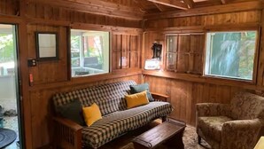 A wooden cabin interior with a checkered sofa, a patterned armchair, and a fireplace.
