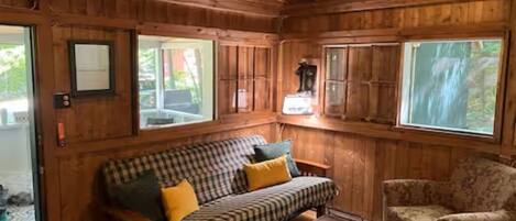 A wooden cabin interior with a checkered sofa, a patterned armchair, and a fireplace.