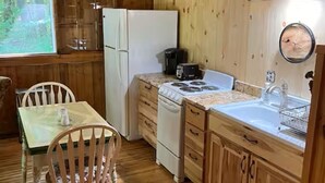 A wooden cabin kitchen with a dining table, chairs, a refrigerator, a stove, and a sink.