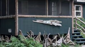 A rustic cabin with a wooden exterior, a porch, and a sign indicating 'Camp 1-2 Many.'