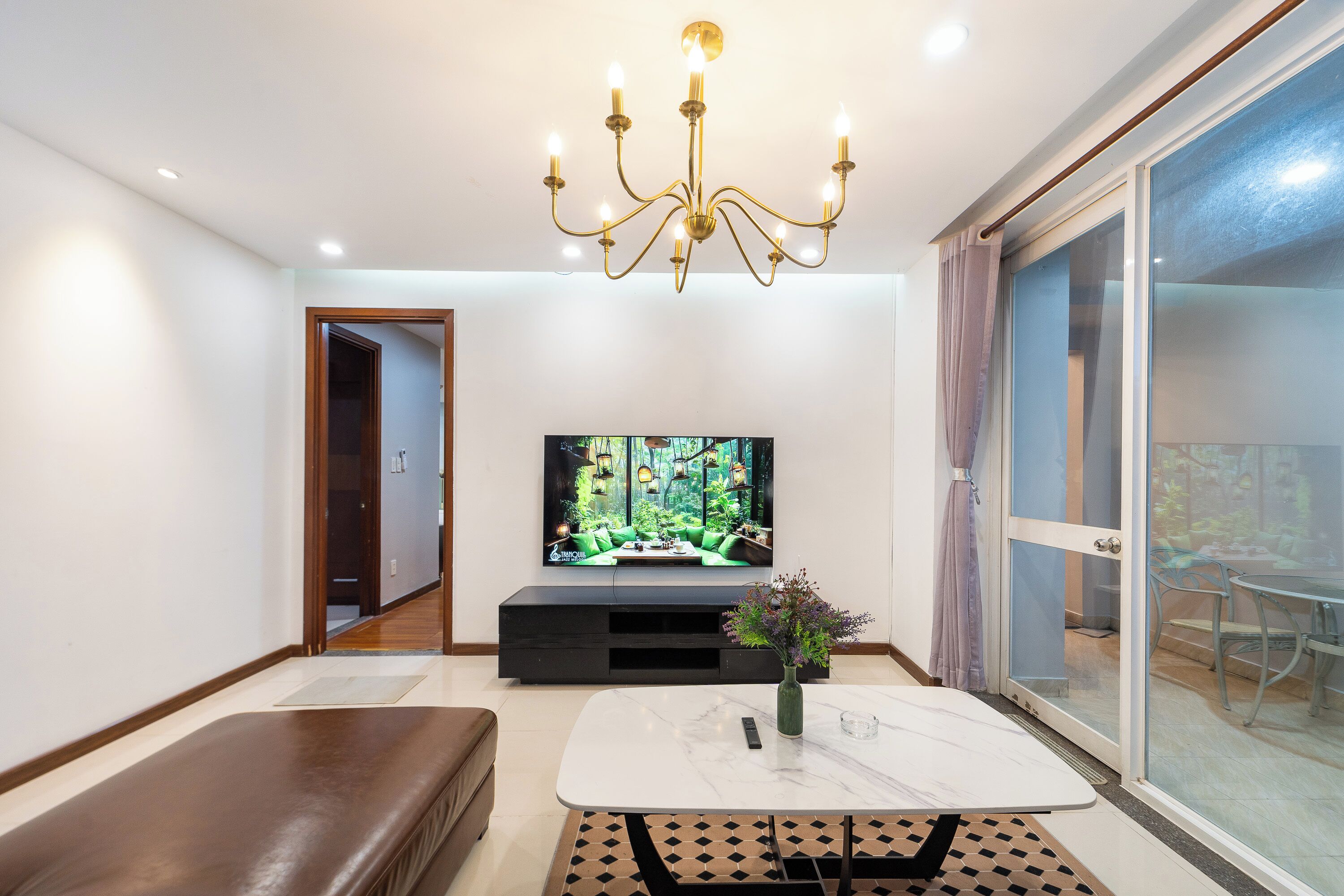 A modern living room with a flat-screen TV, a chandelier, a sofa, and a dining area.