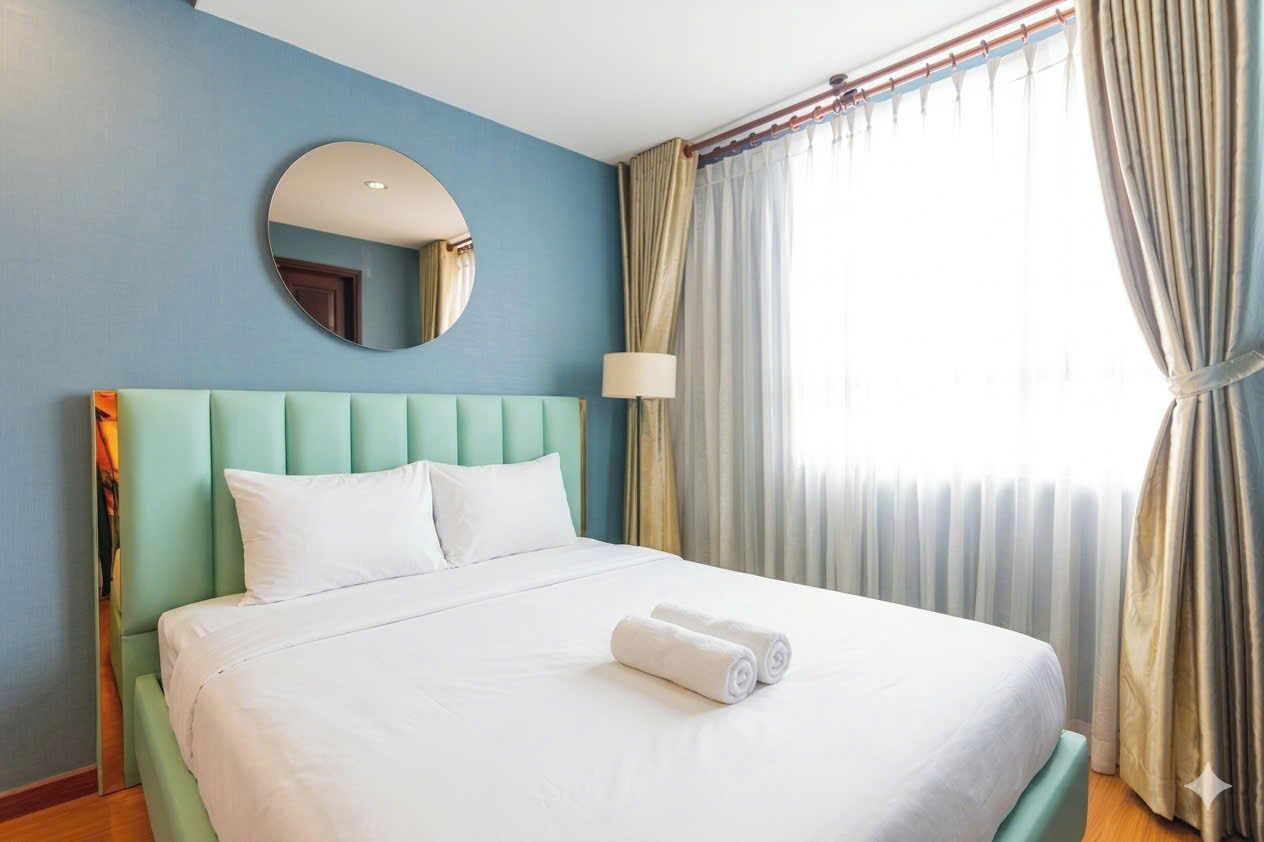 Habitación de hotel con cama, un espejo redondo, una lámpara y cortinas.