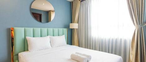Habitación de hotel con cama, un espejo redondo, una lámpara y cortinas.