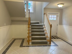 Un escalier avec des rampes en bois, une porte blanche en haut et un luminaire au-dessus.