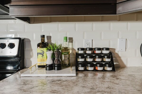 A kitchen counter with a stove, a spice rack, and various bottles. - Sky-View | Modern 2BR Retreat + Balcony (490861) (Sydney)