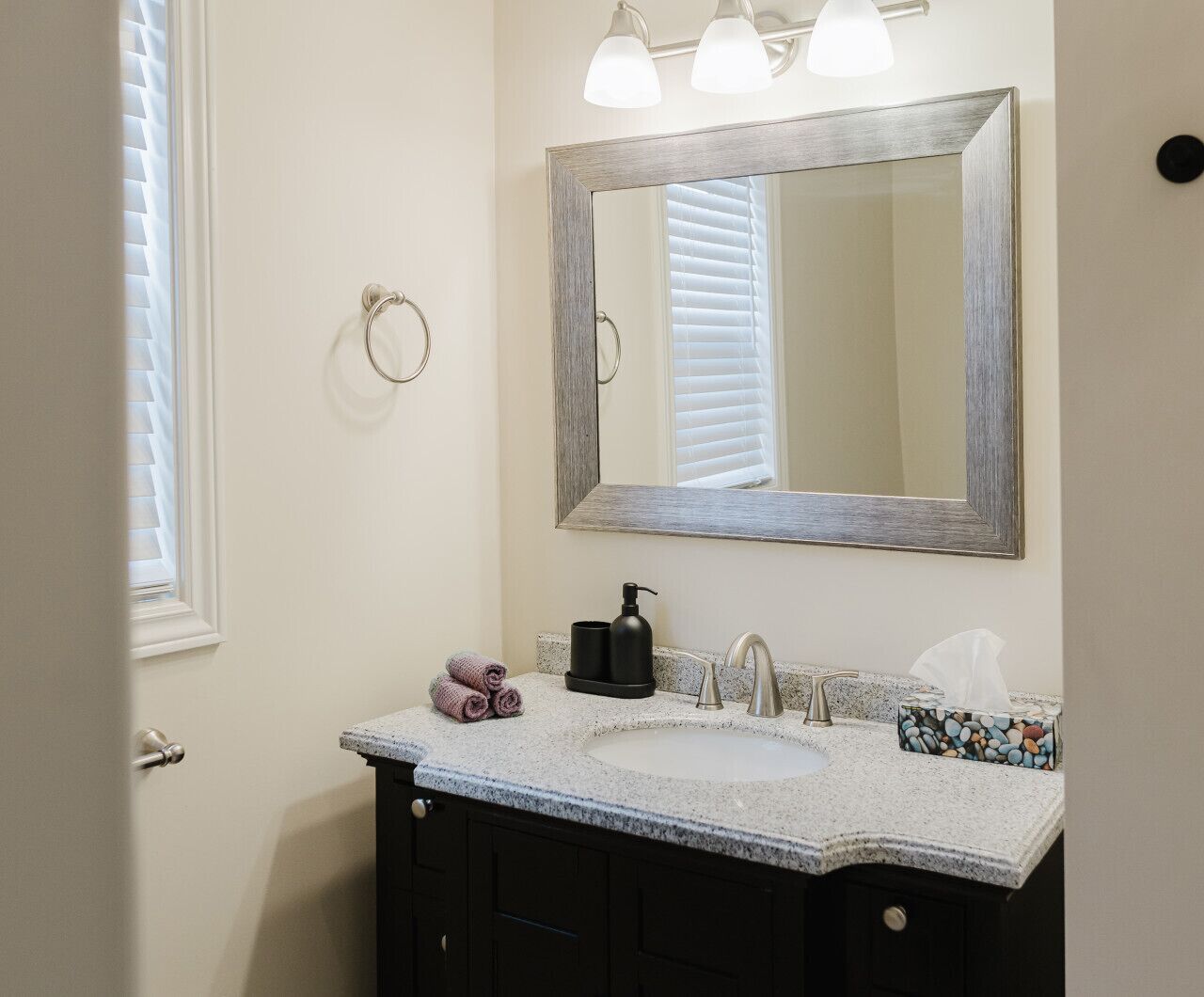 A bathroom with a double sink, a mirror, a towel rack, and a window with blinds.