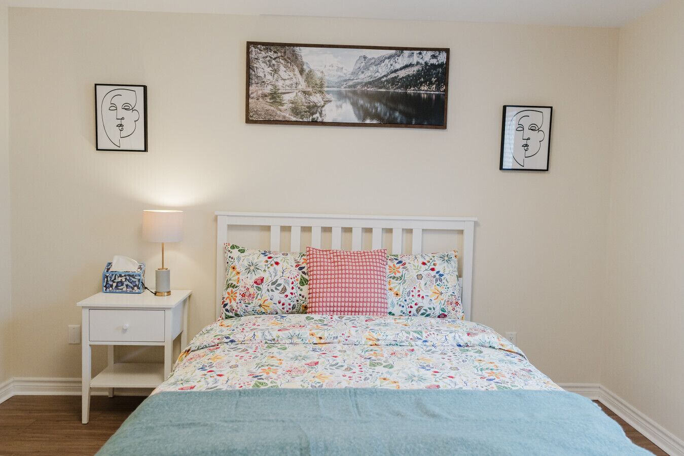 Une chambre à coucher avec un lit, une table de chevet, une lampe et deux tableaux encadrés accrochés au mur.