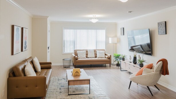 A living room with a sofa, armchair, coffee table, and a TV mounted on the wall. - Garden Suite | Modern 2BR with Private Yard (Sydney)