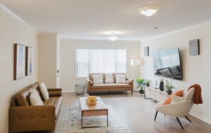 Un salon comprenant un canapé, un fauteuil, une table basse et un téléviseur fixé au mur.