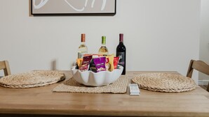 A dining table with a white bowl containing snacks and two bottles of wine, a whiteboard with abstract art, and a thermostat on the wall. - Garden Suite | Modern 2BR with Private Yard (Sydney)