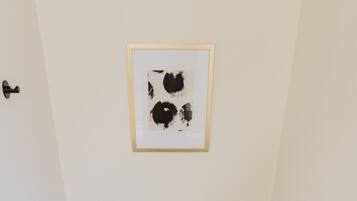 Ein kleines Badezimmer mit Toilette, Mülleimer, einem gerahmten abstrakten Kunstwerk an der Wand und einer Toilettenpapierhalterung.