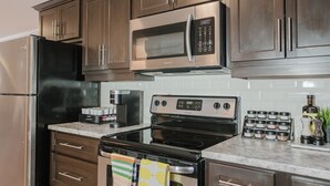A kitchen with stainless steel appliances, wooden cabinets, a coffee maker, and a spice rack. - Garden Suite | Modern 2BR with Private Yard (Sydney)